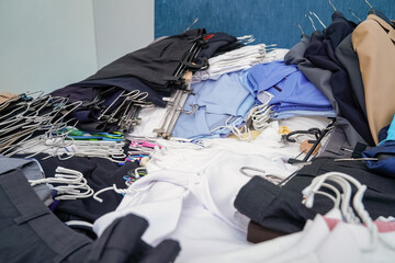 Untidy piles of clothes, arrange on a blue King bed. Women's suits come in a variety of colors, but...