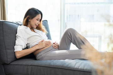 Obraz premium Young Asian pregnancy woman holding tummy with both hands at home. 