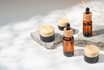 Amber glass dropper with bamboo lid and black jars. Bottle on grey concrete podium for product presentation. Skincare cosmetic with wildflowers. Beauty concept