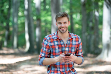 young handsome man in checkered shirt messaging on phone outdoor