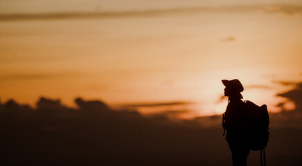 Young woman with backpack hikes in the mountain with a beautiful view through the sunset with warm red light. Blurred silhouette background.