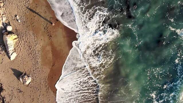 Birds Eye view of Cambria Beach. Drone Footage at Sunset of waves crashing in at Californian shoreline. A kid collecting shells at beach. Roadtrip at Westcoast at Highway One.