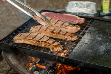Beef steaks grilling on a cast iron grlill plate on a camp fire. Campfire cooking. Outdoor BBQ