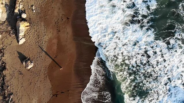 Birds Eye view of Cambria Beach. Drone Footage at Sunset of waves crashing in at Californian shoreline. A kid walking at the beach. Roadtrip at Westcoast at Highway One.