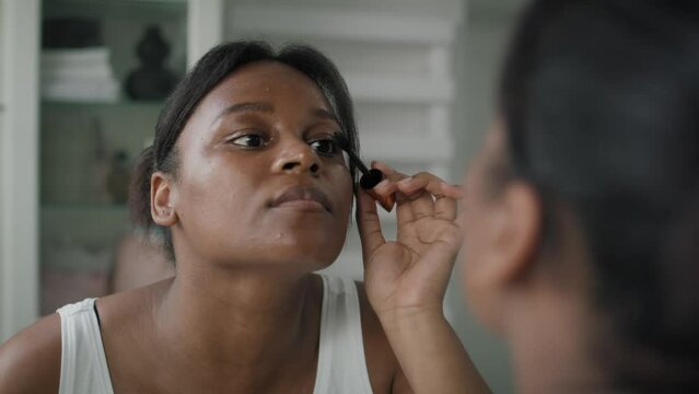 African-American woman applying eyelash in the mirror reflection. Shot with RED helium camera in 4K.  