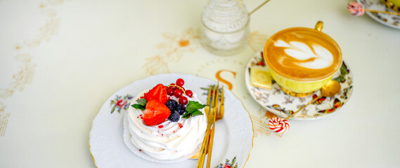 Obraz premium Banner with sweet meringue dessert decorated with strawberries, blackberries and red currants and a cup of coffee. Elegant service. Morning concept.