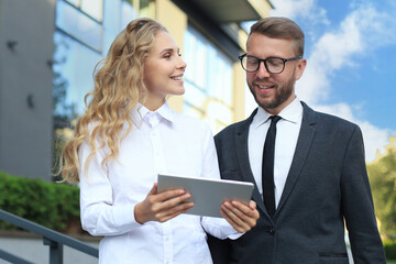 Office colleagues talking outdoors near the office building, discussing new project, holding digital tablet.