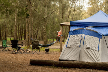Family tent at the camping site. Camping chairs, campfire firepit and hammock. Travel tourism...