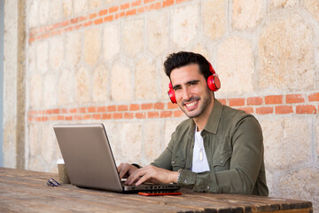 Man looking at camera while working with a laptop and using headphones outdoors