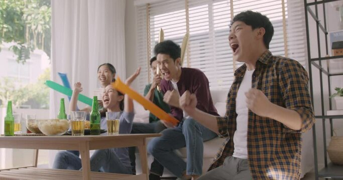 Group of young adult friend man and woman asia people sit at sofa couch joy chanting party fun game world cup live TV at home eat snack bowl drink beer bottle glass jump mad happy win exult face.