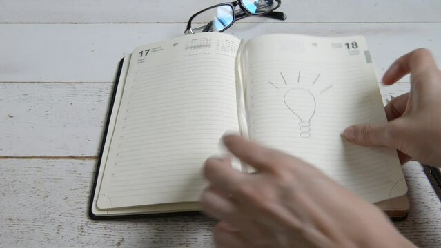 Women's hands leaf through a notebook and leave open a page with a picture of a light bulb, the concept of the idea