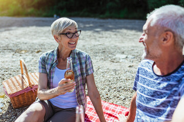 Cute senior couple enjoying picnic time on the riverside.