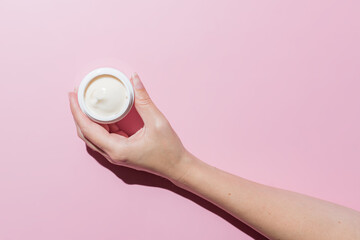 Woman Hand holding an open cosmetic cream container on pink background. Mockup with space for text. Branding presentation of cosmetic product