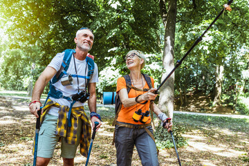 Obraz premium Senior couple hiking in forest wearing backpacks and hiking poles. Nordic walking, trekking. Healthy lifestyle.