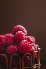 Sweet raspberries in a wicker basket on a wooden background. Organic food and clean eating concept.