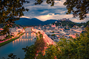 Illuminated streets in Salzburg town. Aerial summer view of Old City, birthplace of famed composer Mozart and Salzach river. Gloomy sunset in Eastern AlpsAustria, Europe. Traveling concept background. - obrazy, fototapety, plakaty