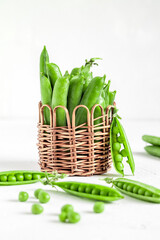 Wicker basket with fesh green pods and peas on a white background.
