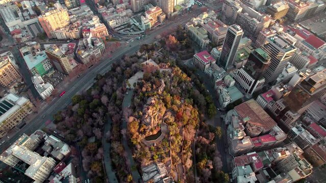 Aerial dolly in of Santa Lucia Hill covered in autumnal trees, traffic in Alameda avenue and Santiago buildings in back, Chile