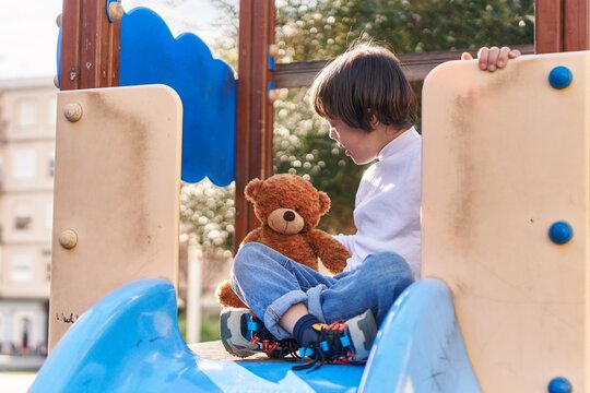 Down syndrome kid playing with teddy bear on slide at park