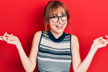 Redhead young woman wearing casual clothes and glasses celebrating victory with happy smile and winner expression with raised hands