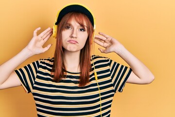 Fototapeta premium Redhead young woman listening to music using headphones depressed and worry for distress, crying angry and afraid. sad expression.