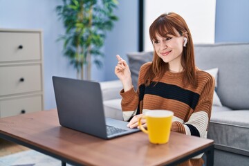 Young beautiful woman using computer laptop doing video call smiling happy pointing with hand and finger to the side