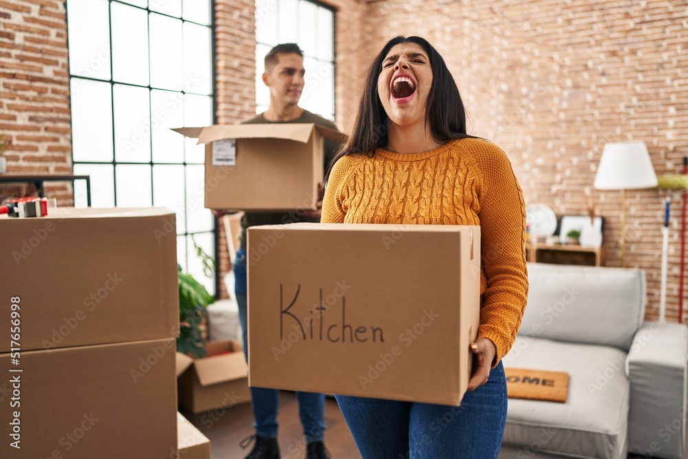 Poster young couple moving to a new home with cardboard boxes angry and mad screaming frustrated and furiou