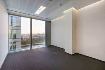 A bright office room without furniture, with a brown carpet and a panoramic window.