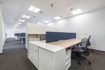 An open space of a bright office with white furniture in the work areas.