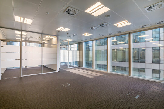 An empty office space with brown carpet, panoramic windows and glass partitions.