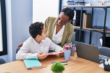 African american mother and son using laptop and reading book at office