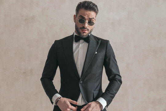 elegant businessman in black tuxedo wearing sunglasses and posing