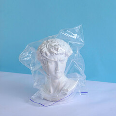 The head of an antique David statue and a plastic bag on a pastel background as a concept of...