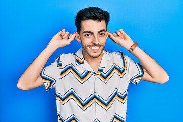 Young hispanic man wearing casual clothes smiling pulling ears with fingers, funny gesture....