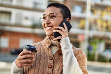 Young hispanic woman with short hair smiling happy drinking a cup of coffee and talking on the phone