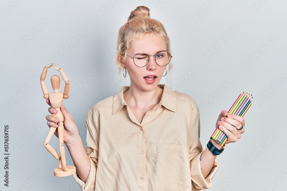 Poster beautiful caucasian woman with blond hair holding small wooden manikin pencils winking looking at th