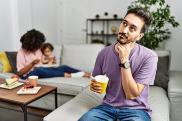 Hispanic father of interracial family drinking a cup coffee with hand on chin thinking about question, pensive expression. smiling with thoughtful face. doubt concept.