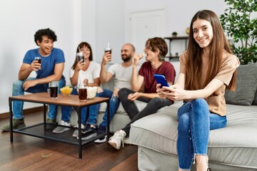 Group of young friends having party sitting on the sofa at home. Woman smiling happy using smartphone at home.