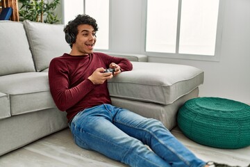 Young hispanic man playing video game sitting on the floor at home.