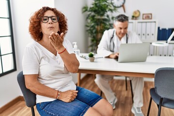 Senior woman sitting at doctor appointment looking at the camera blowing a kiss with hand on air being lovely and sexy. love expression.