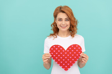 cheerful redhead woman hold red heart on blue background