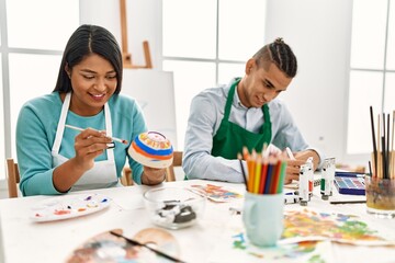 Young latin painter couple smiling happy painting sitting on the table at art studio