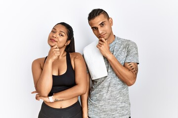 Naklejka premium Young latin couple wearing sportswear standing over isolated background looking confident at the camera smiling with crossed arms and hand raised on chin. thinking positive.