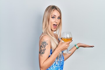 Young beautiful caucasian woman drinking a glass of white wine pointing aside with hands open palms showing copy space, presenting advertisement smiling excited happy