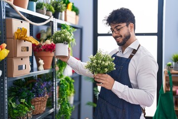 Young hispanic man florist smiling confident holding plants at florist shop