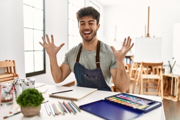 Young hispanic man at art studio celebrating mad and crazy for success with arms raised and closed eyes screaming excited. winner concept