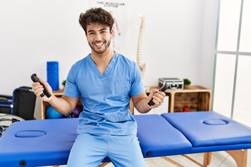 Young hispanic man wearing physio therapist uniform using grip hand at clinic