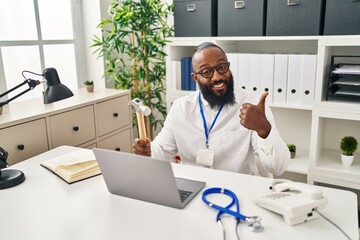 African american man working at medical clinic holding hammer smiling happy and positive, thumb up doing excellent and approval sign