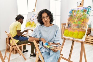 Young hispanic woman at art studio looking sleepy and tired, exhausted for fatigue and hangover, lazy eyes in the morning.