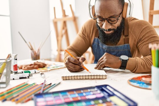 Young african american artist man using headphones drawing at art studio.